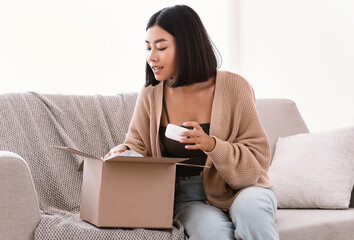 Wall Mural - Asian woman unpacking parcel with beauty box