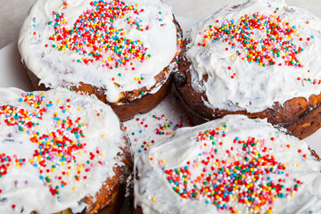 Wall Mural - Top view of four freshly baked Easter cakes close-up with traditional confectionery decoration - frozen white icing sprinkled with multicolored round confetti, a treat for a christian church holiday.