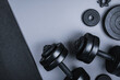 Top view of black dumbbells and different weight plates and textured mat on grey background. Flat lay.