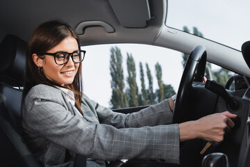  businesswoman in eyeglasses smiling while starting car