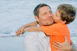 © Maria - Child son hugs and kisses his father tightly while walking along the beach. Portrait of a cheerful and happy family. Friendly family concept.