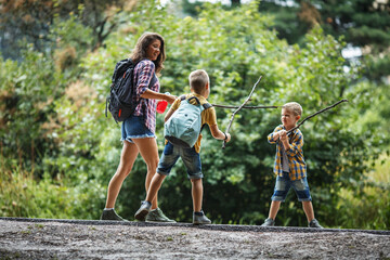 Wall Mural - mother and her little sons hiking trough forest .making fun and fight with wooden sticks.