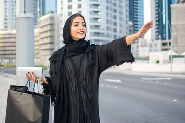 Wall Mural - Middle eastern Emirati woman in traditional clothes catching a taxi on the city street.