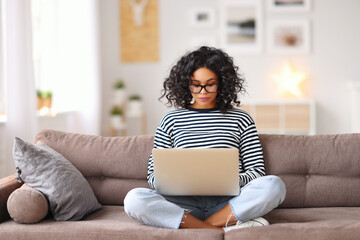 Wall Mural - Smart ethnic woman using laptop on sofa.