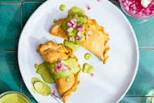 Chicken And Black Bean Empanadas Garnish With Green Sauce And Pickled Onions Served On Plate