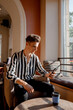 © ibilyk13 - Young man sitting at a table in a cafe. Guy with a phone in a cafe on a chair. Stylish guy spends time with phone and coffee.