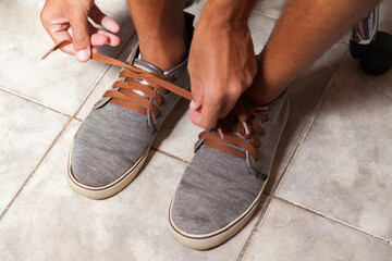 Detail of the hands of a young Brazilian man tying the tennis shoe to practice walking in the neighborhood. Footwear concept. Sport concept.