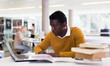 © JackF - Serious african-american man reading book and working on laptop in public library. High quality photo