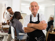 © JackF - Portrait of professional aged barber standing with crossed arms in modern hair salon..