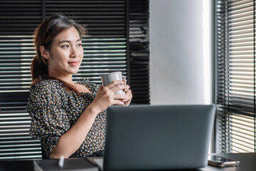 Wall Mural - Asian woman drinking coffee and laptop computer in the morning at office.