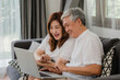 © tirachard - Asian senior couple using laptop at home. Asian Senior Chinese grandparents, surf the Internet to check social media while lying on sofa in living room at home concept.