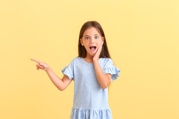 Poster - Surprised little girl pointing on something on color background