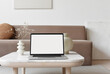 © kite_rin - Blank screen laptop computer mockup over white modern living room design. View of modern scandinavian style interior with sofa. Home staging and minimalism concept