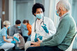 © Drazen - African American doctor wearing face mask while talking to senior patient at medical clinic.