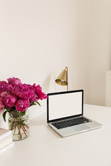 Wall Mural - Office desk table workspace with blank copy space mock up laptop screen. Modern stylish home interior design with pink peonies flower bouquet. Front view blog, social media, website hero template.