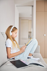 Wall Mural - Girl with a textbook folding her legs on a couch