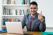 © Daniel Ernst - Laughing mexican businessman at computer showing thumb up at office