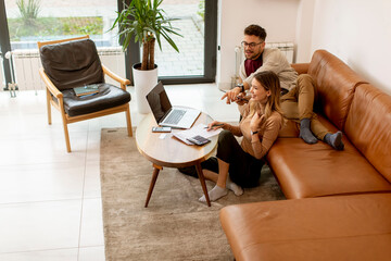 Young woman using laptop and young man using digital tablet while sitting on sofa at home