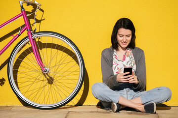 Wall Mural - smiling young woman looking phone next to a bike