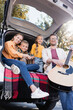© LIGHTFIELD STUDIOS - Smiling kids sitting near parents with acoustic guitar in trunk of car
