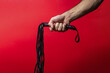 Leather whip. A man's hand holds a leather whip on a red background. BDSM accessories