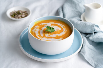 Wall Mural - Pumpkin soup with coconut milk in blue bowl, vegetarian dish, healthy dieting food on white tablecloth, side view