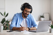 © Prostock-studio - Western Guy Wearing Headphones Studying Online With Laptop At Home, Taking Notes