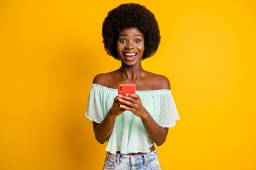 Sticker - Photo portrait of excited girl with open mouth holding phone in two hands isolated on vivid yellow colored background