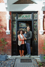 Portrait Happy Couple With Baby Daughter At Sunny House Front Door
