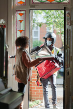 Woman Receiving Pizza From Delivery Man In Face Mask At Front Door