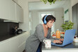 © Paul Bradbury/Caia Image - Woman with headphones working from home at laptop in kitchen