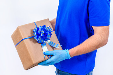 Safe contactless remote delivery of holiday gifts during the coronavirus pandemic. Close up. Courier hand in protective medical gloves holds a beautiful gift box with a bow on a white background