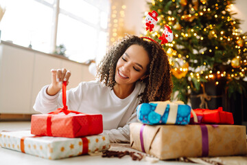 Happy lady with gifts near the Christmas tree. Young woman posing with presents in Christmas interior design. Fashion, celebration, holidays concept.