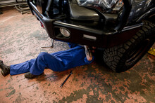 Male Auto Mechanic Working Under Modified SUV In Garage