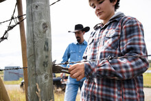 Rancher Father And Son Fixing Barbed Wire Fence On Sunny Ranch