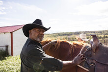 Portrait Confident Male Farmer Preparing Saddle On Horse On Sunny Farm