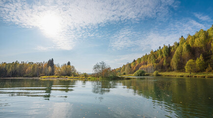 Canvas Print - Autumn forest trees are reflected in the river water of the panoramic landscape. Blue sky with clouds.