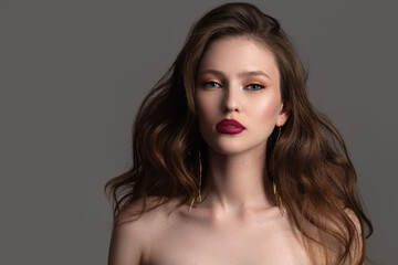 Portrait of a beautiful young woman with red lipstick, makeup and gold earrings on a dark background