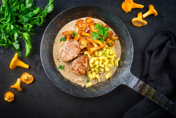 Wall Mural - Modern style traditional fried pork filet medaillons in cream sauce with chanterelle mushrooms and spaetzle offered as top view on a rustic wrought iron skillet