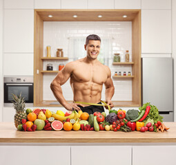 Sticker - Man measuring his waist and posing with a pile of healthy fruits and vegetables on a counter