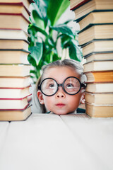 Kids development and education concept. Little girl in glasses between two books towers with copy space.