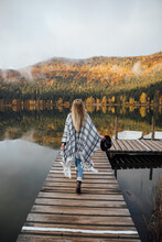 Young Hipster Blonde Woman Standing On The Pier Near The Wonderful Mountain Lake In Autumn Season At Sunrise.