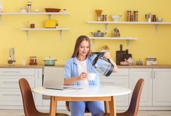 Poster - Young woman pouring boiled water from electric kettle into cup in kitchen