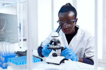 Wall Mural - african chemist doing investigation using microscope analysing sample on glass slide. black healthca