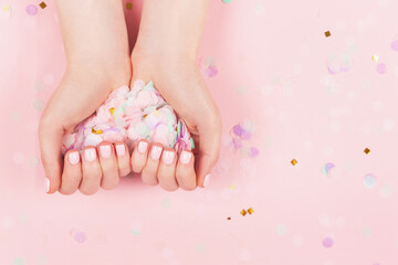 Wall Mural - Manicure and nail care concept. Woman hands are holding pastel confetti. Perfect pastel pink nail polish. Party, holidays or celebration vibes.