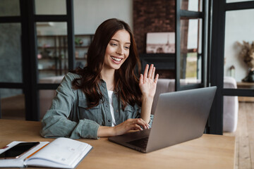 Beautiful smiling woman waving hand and working with laptop