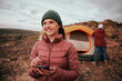 © StratfordProductions - Portrait of happy woman holding smartphone looking away during camping while man building tent in background