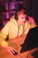 Wall Mural - Young man using headset while gaming on computer on blurred foreground