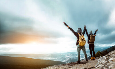 Wall Mural - Hikers with arms up celebrating success on the top of a mountain at sunset - Couple hiking rock - Success, teamwork and sport concept