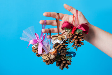 hand hold pine cone toys decoration for a Christmas tree with a red ribbon bow, eco friendly decor hanging gift for the New Year holidays isolated on a blue background.